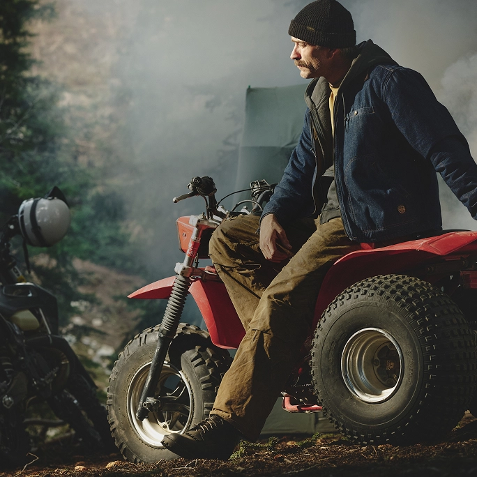 Man seated on a red all-terrain vehicle in a misty forest