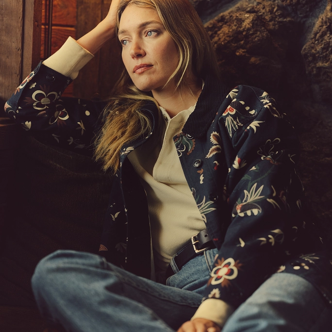 Woman in a navy embroidered jacket resting her head on her hand