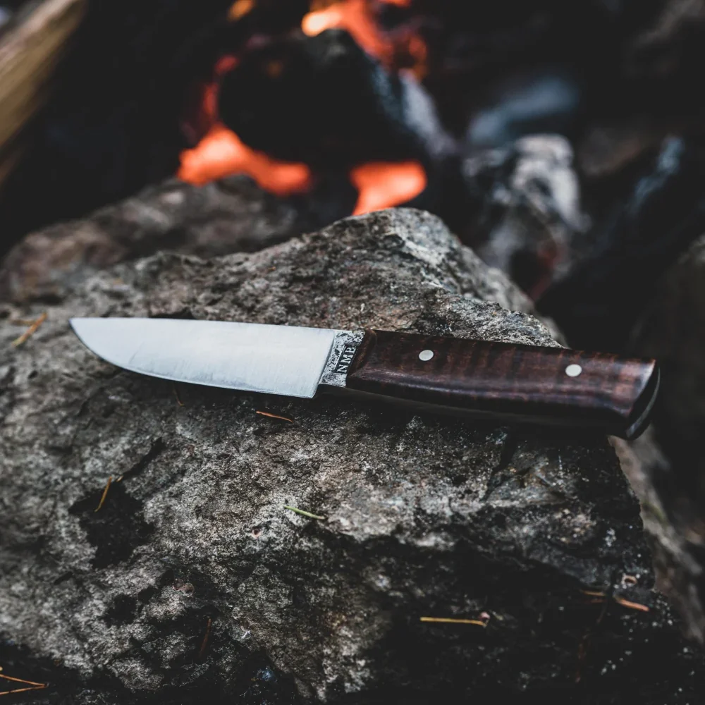 A knife resting on a rock beside a campfire