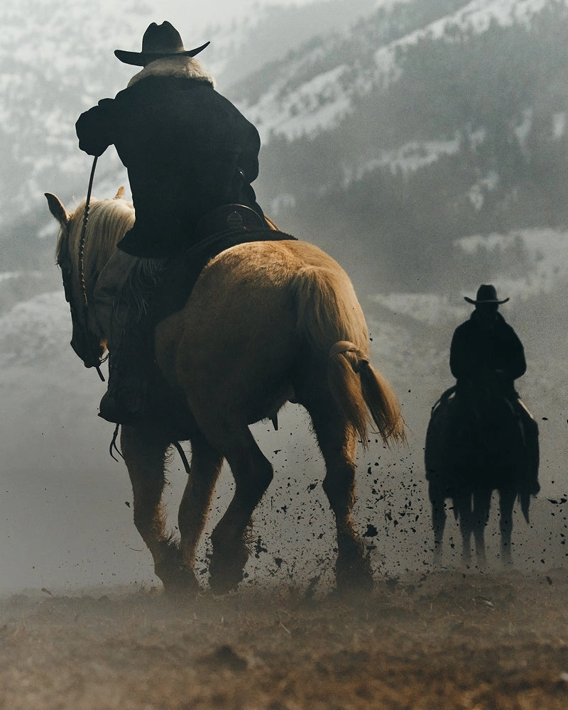 A rider on horseback with a second rider behind in a cloud of dust