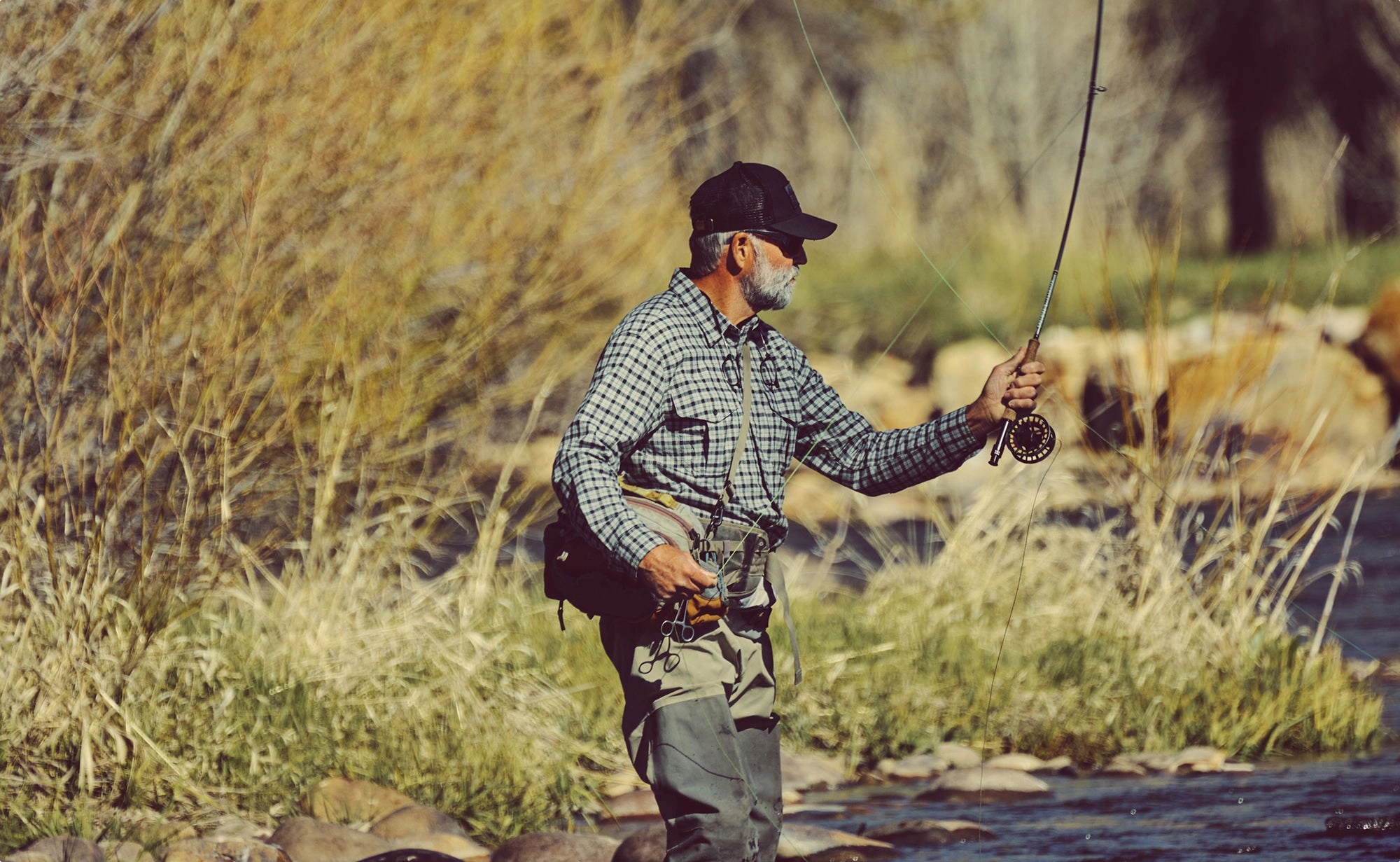 Angler casting a fly rod in a river with the line arcing overhead