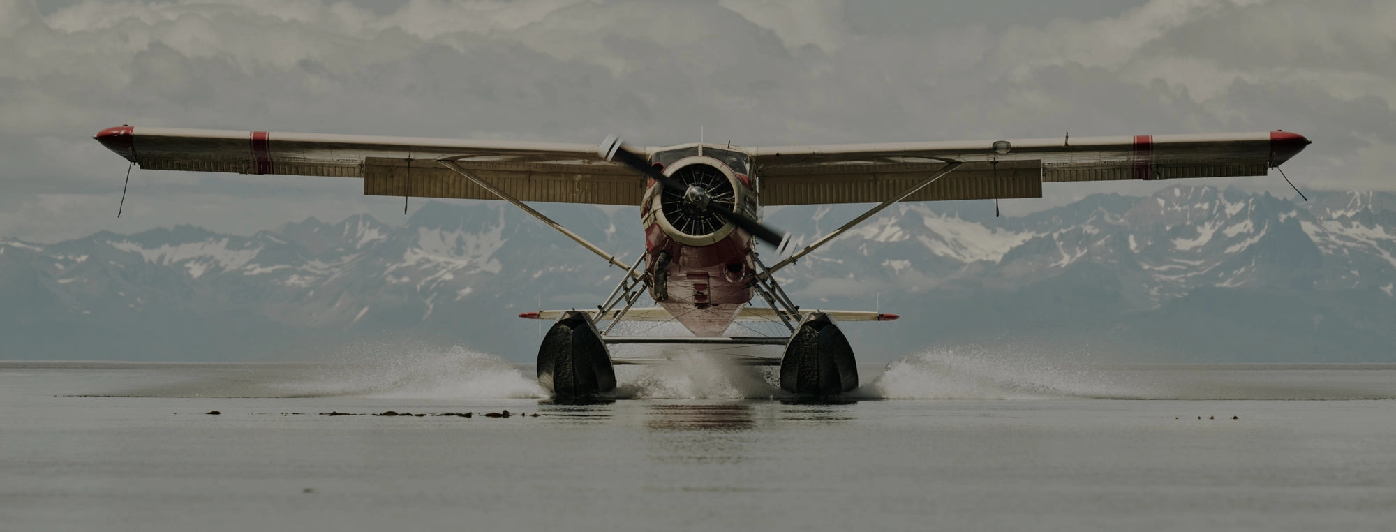 A floatplane skimming the water in front of snowy mountains