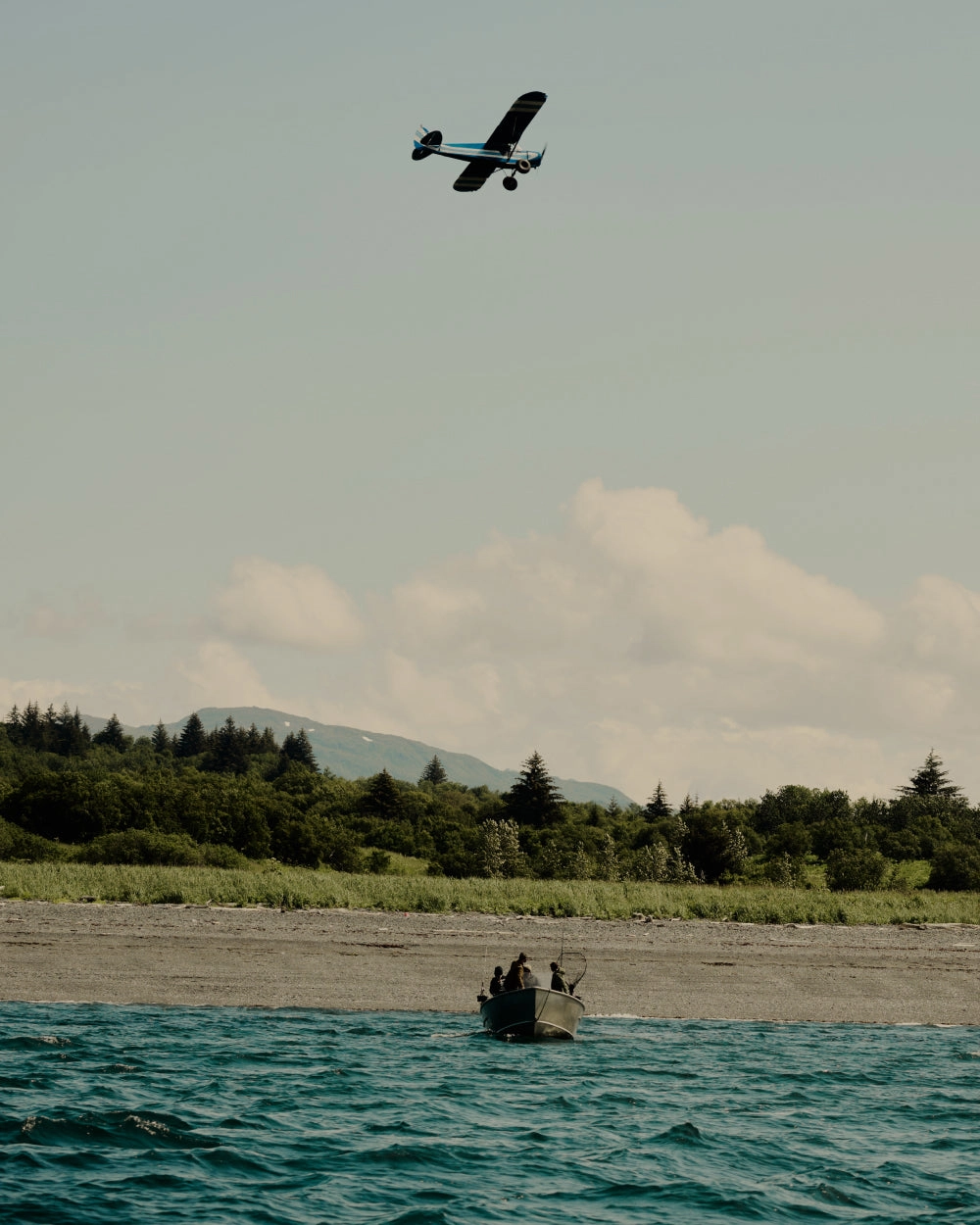 A floatplane in the sky above a small boat on a green lake