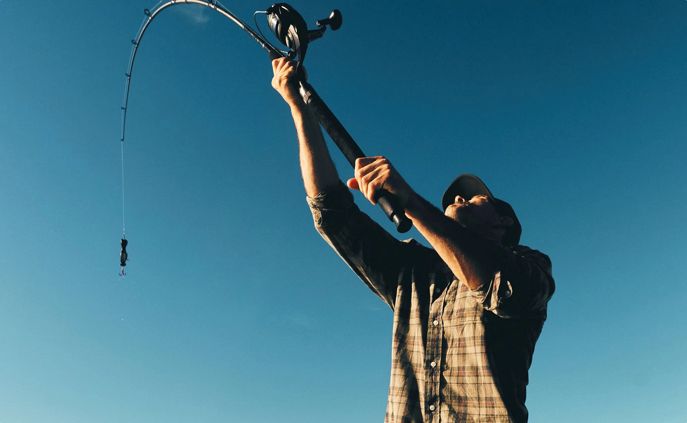 Angler against a deep blue sky holding a bent fishing rod